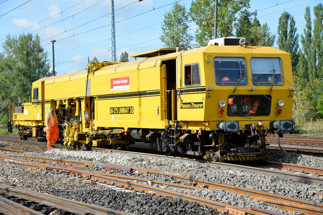 Bahnarbeiter geht neben einer Gleisstopfmaschine her